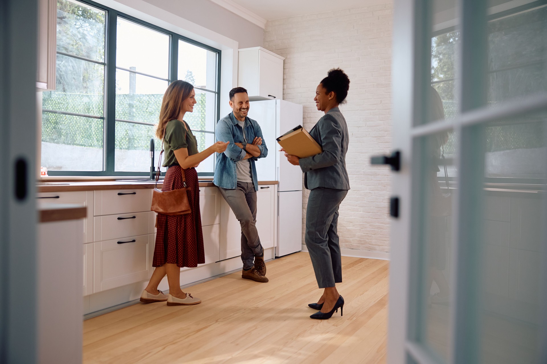 Happy black real estate agent and a couple in the kitchen of a new house.